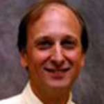 Picture of a smiling man wearing a pale yellow shirt in front of a gray background, Don Radford