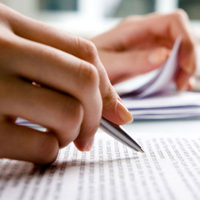 Close-up of hands holding a pen and reviewing printed text on a document.